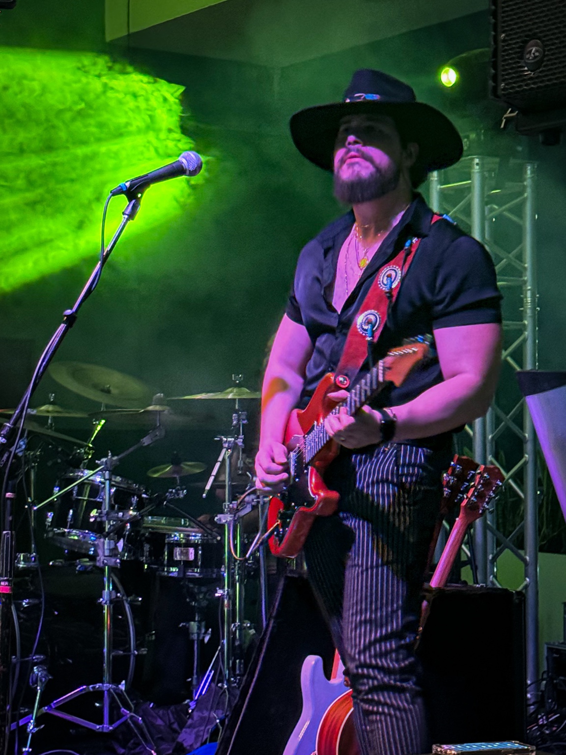 Will Plus playing electric guitar beside a microphone under green concert lighting