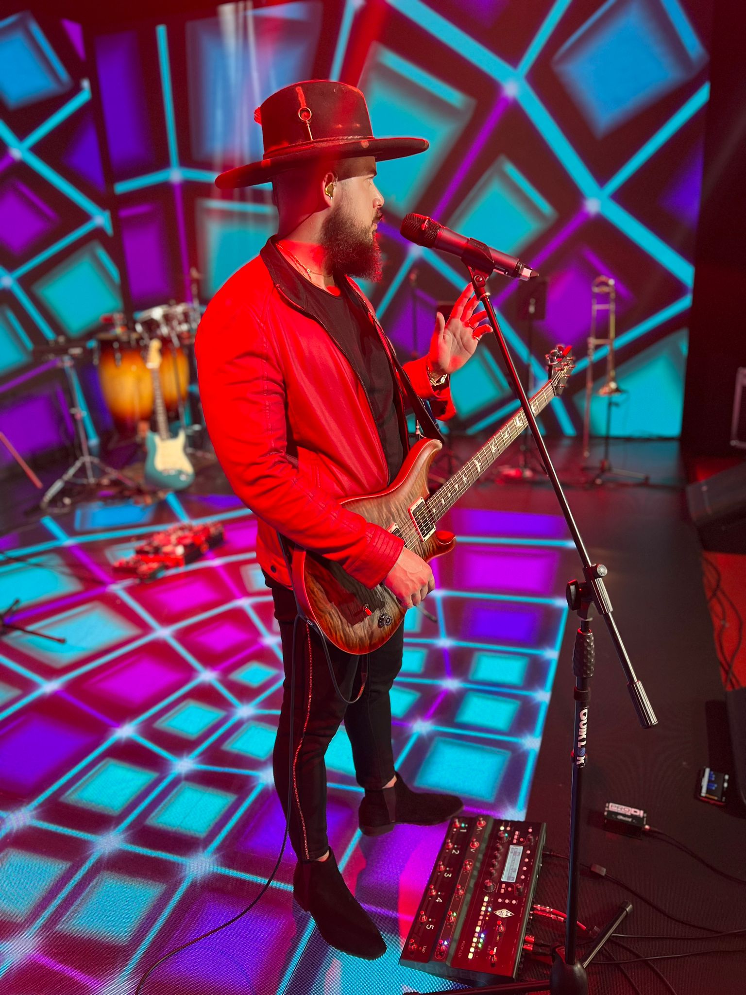 Will Plus in a red jacket with electric guitar at the microphone on a colorful stage